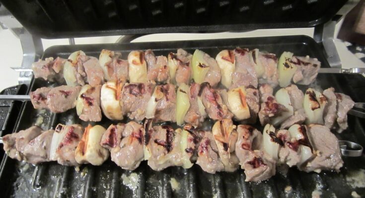 Three souvlaki skewers on a black grill