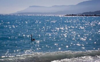 A beach in the Mediterranean sea. A woman can be observed swimming.