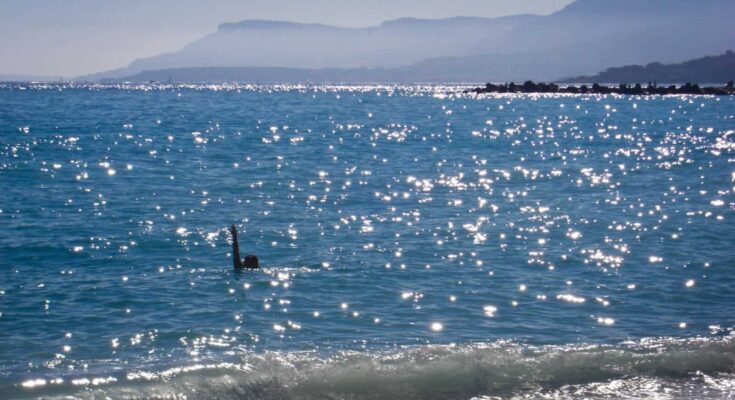 A beach in the Mediterranean sea. A woman can be observed swimming.